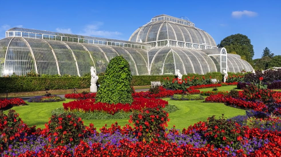 The outside of the Palm House in Kew Gardens showing flower beds in red bloom